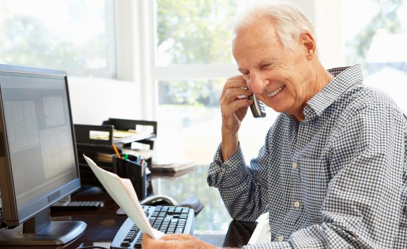 Un hombre mayor habla por teléfono mientras revisa unos documentos