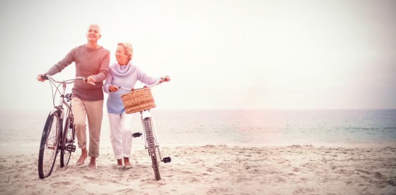 Una pareja de personas mayores andan con unas bicicletas en la mano en la playa