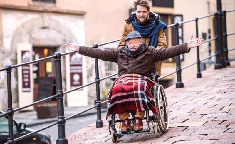 Un hombre mayor en silla de ruedas y un joven bajan por una calle