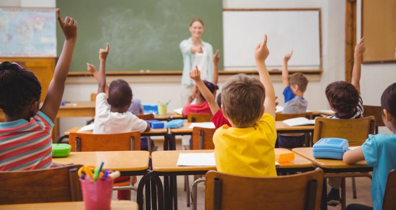 Fotografía de una clase con muchos niños levantando la mano
