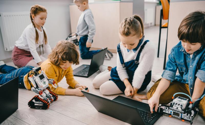 Varios niños programan juntos entre varios ordenadores y robots