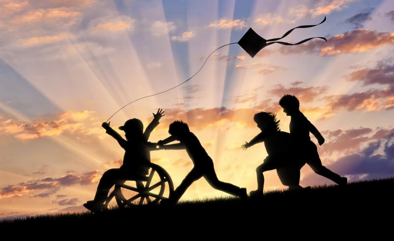 Unos niños juegan a la puesta del sol con una cometa que lleva un niño en silla de ruedas