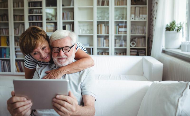 Una pareja de personas mayores utiliza una tableta en su salón