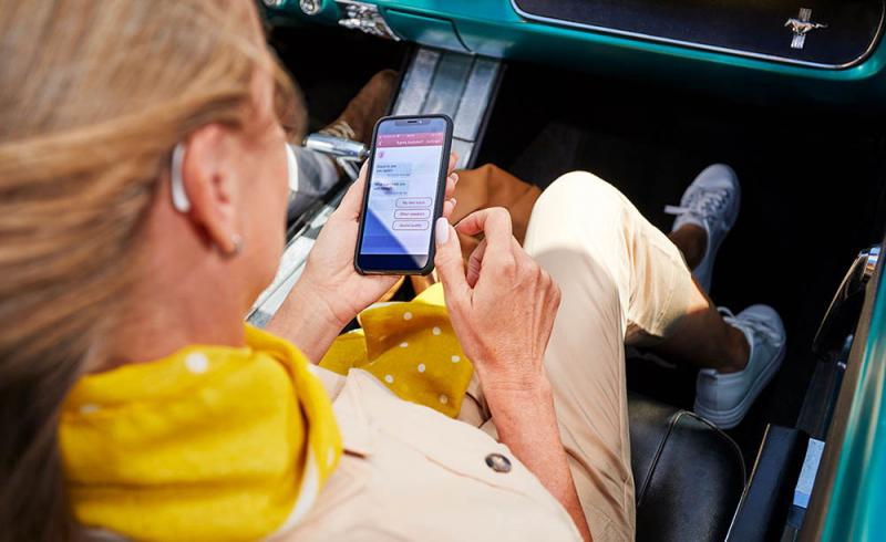 Una mujer configura su audífono Signia Styletto X con el móvil sentada en un coche