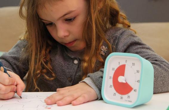 Una niña dibuja al lado de un reloj Time Timer
