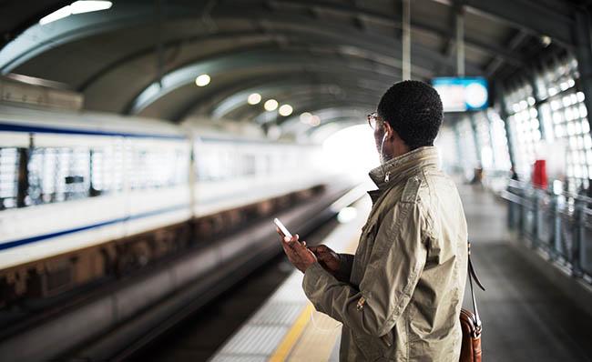 Una persona espera en un andén la llegada de un tren mientras utiliza el móvil