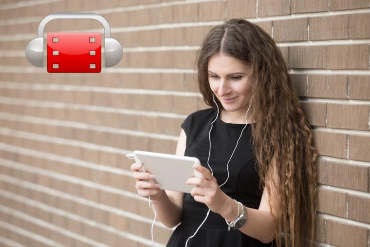 Una mujer ve la televisi&oacute;n en una tableta mientras escucha por unos auriculares y aparece el logo de AudescMobile