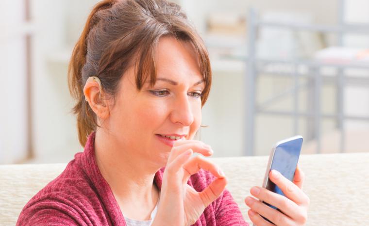 Una mujer con aud&iacute;fono utiliza un tel&eacute;fono m&oacute;vil
