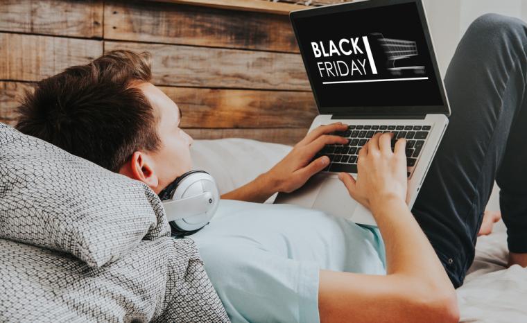 Un joven tumbado en un sof&aacute; compra en el Black Friday con su ordenador