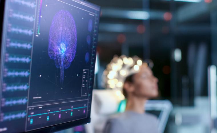 Imagen de una pantalla mostrando se&ntilde;ales cerebrales de una mujer sentada al fondo