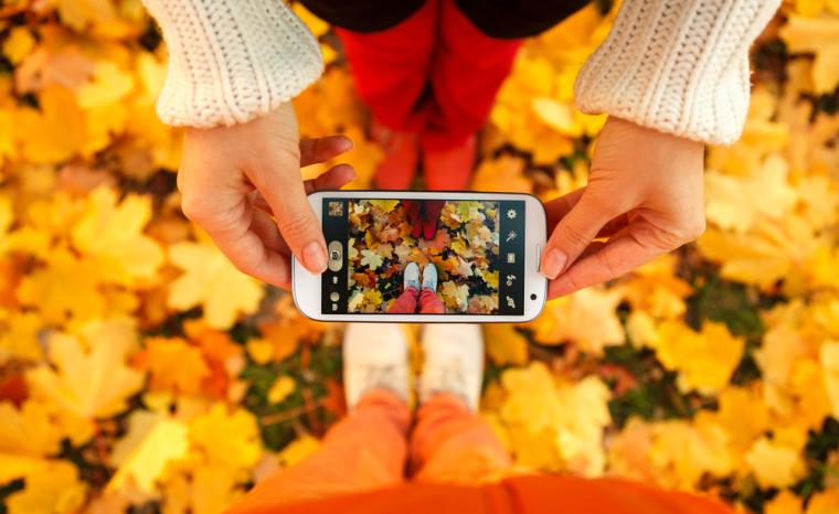 Dos ni&ntilde;os se fotograf&iacute;an los pies con un smartphone, en un suelo lleno de hojas