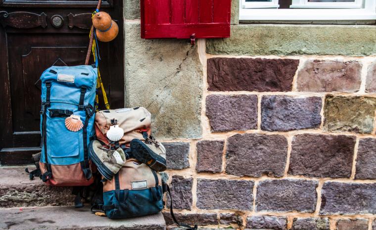 Fotograf&iacute;a de dos mochilas apoyadas sobre la pared de una fachada en el trayecto del Camino de Santiago
