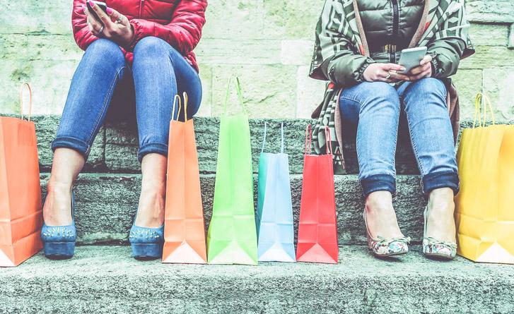 Varias mujeres con bolsas de compra sentadas utilizando su tel&eacute;fono m&oacute;vil
