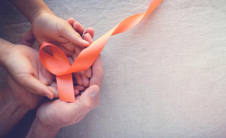 Las manos de una persona mayor y un ni&ntilde;o sujetan un lazo naranja con motivo del D&iacute;a Mundial de la Esclerosis M&uacute;ltiple