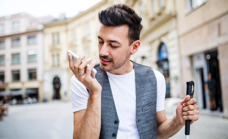 Un joven con discapacidad visual utiliza su tel&eacute;fono m&oacute;vil mientras pasea