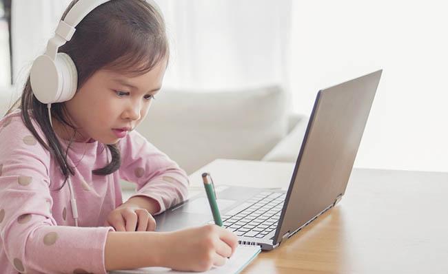 Una ni&ntilde;a participa en tareas educativas desde su casa junto a un ordenador port&aacute;til