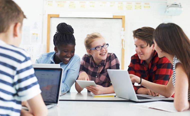 Varios estudiantes utilizan ordenadores y tabletas en un aula
