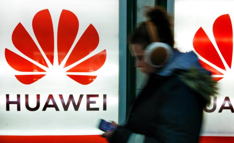 Una mujer con auriculares camina por delante de unos letreros de Huawei