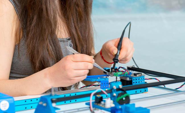 Una joven suelda distintas partes de un dispositivo tecnol&oacute;gico
