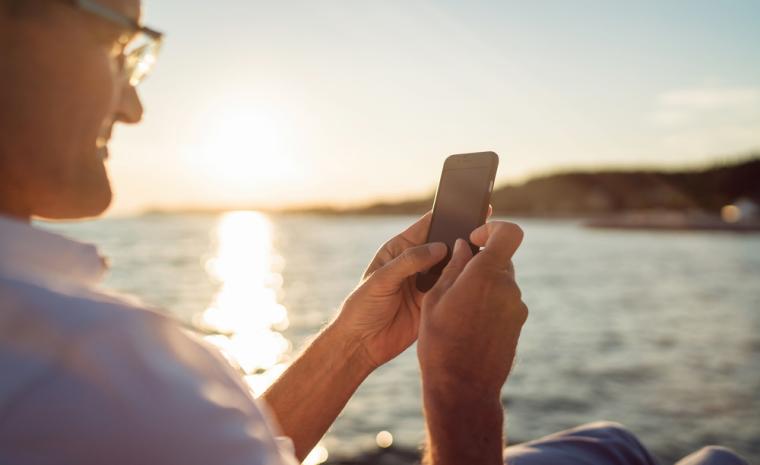 Un hombre utiliza su tel&eacute;fono m&oacute;vil con el mar al fondo