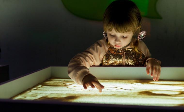 Una ni&ntilde;a experimenta con la arena sobre una mesa de luz