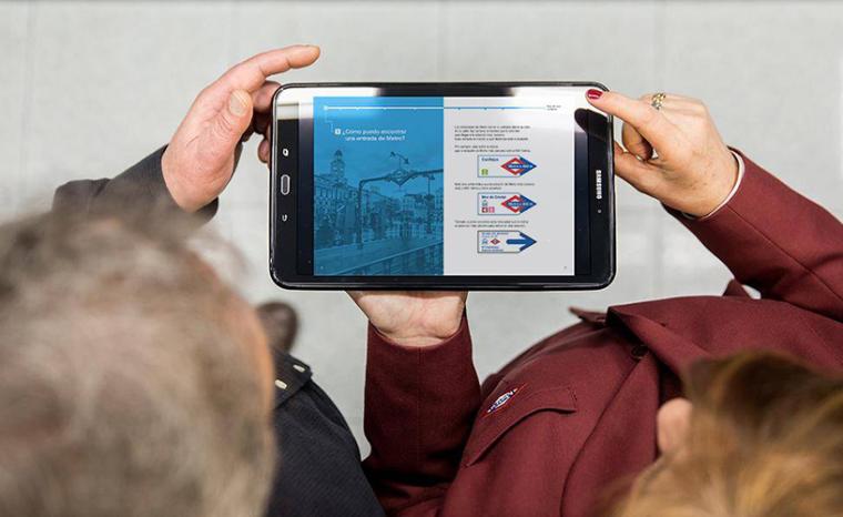 Una empleada de Metro de Madrid ayuda a un usuario a utilizar el suburbano mostrando la gu&iacute;a en lectura f&aacute;cil en una tableta
