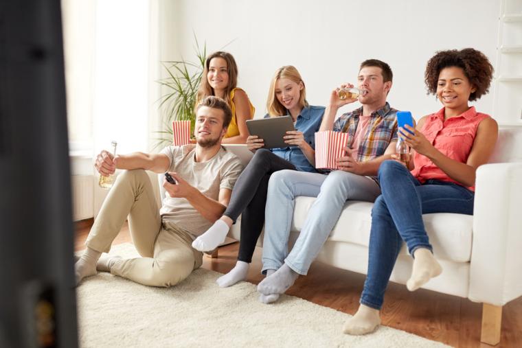 Varias personas j&oacute;venes ven la televisi&oacute;n mientras utilizan smartphones y tabletas