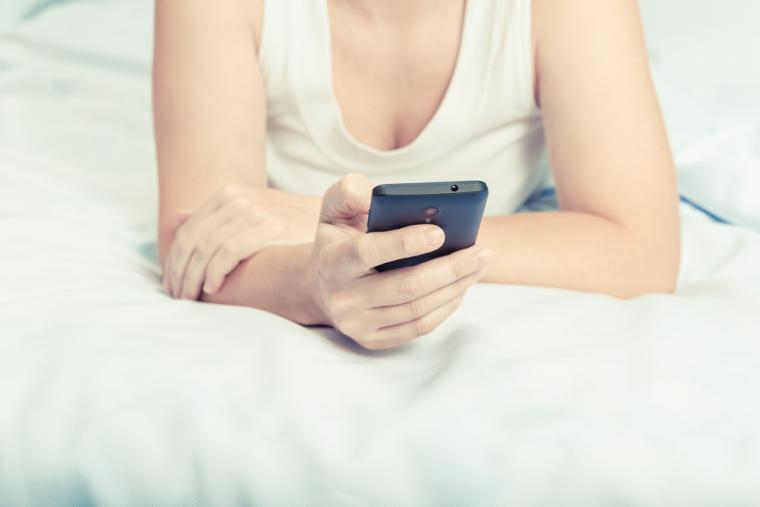 Una mujer utiliza su tel&eacute;fono m&oacute;vil en la cama