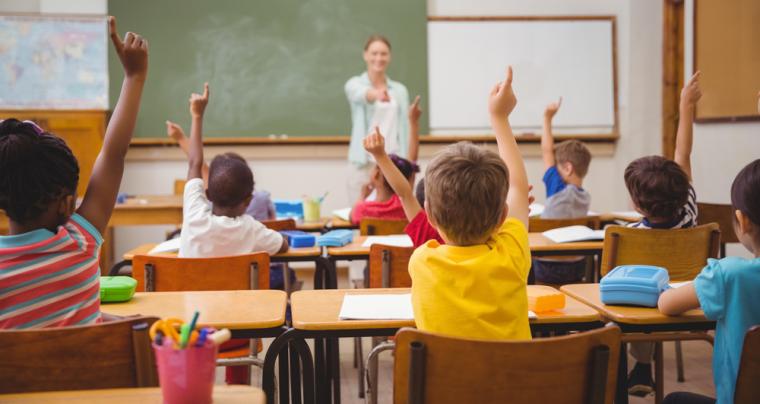 Fotograf&iacute;a de una clase con muchos ni&ntilde;os levantando la mano
