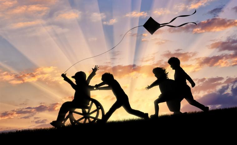 Unos ni&ntilde;os juegan a la puesta del sol con una cometa que lleva un ni&ntilde;o en silla de ruedas