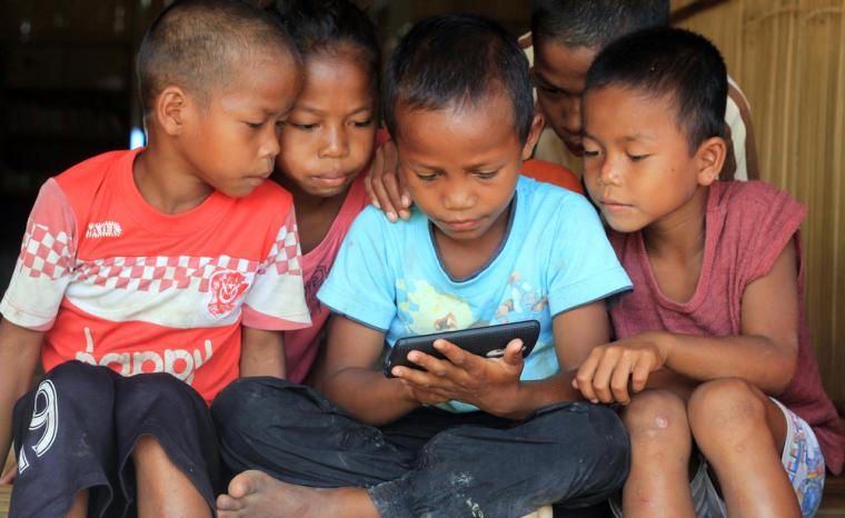 Varios ni&ntilde;os sentados miran un tel&eacute;fono m&oacute;vil