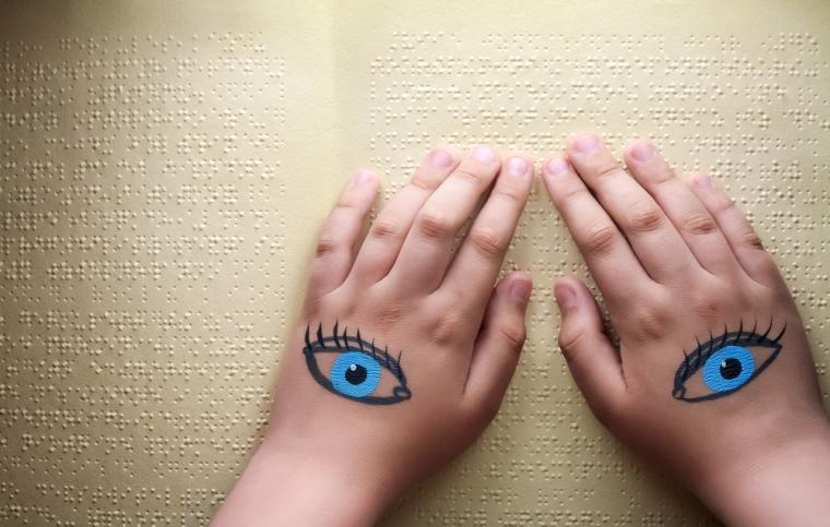 Unas manos con un dibujo de unos ojos leen un texto en braille
