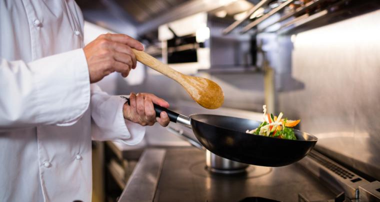 Un cocinero saltea verduras en la cocina de un restaurante