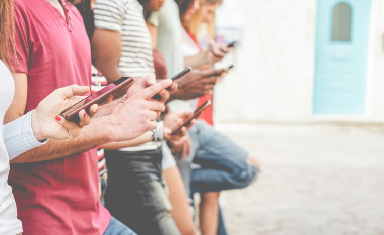 Varios adolescentes apoyados en una pared utilizan sus tel&eacute;fonos m&oacute;viles