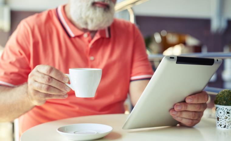 Un hombre mayor utiliza una tableta mientras toma un caf&eacute;
