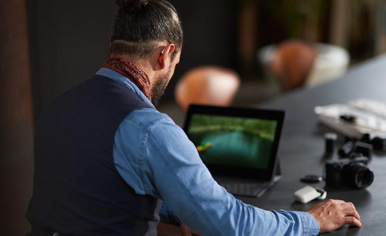 Un hombre utiliza los aud&iacute;fonos Styletto Connect mientras maneja un ordenador port&aacute;til