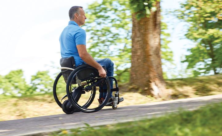 Una persona utiliza SmartDrive en su silla de ruedas subiendo un camino entre &aacute;rboles