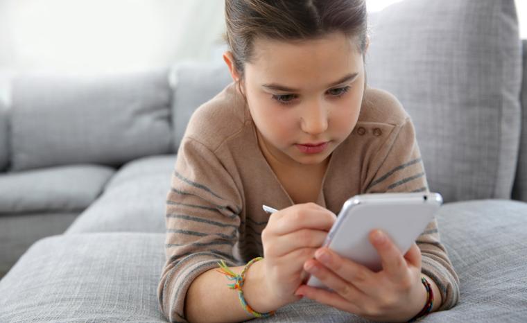 Una ni&ntilde;a utiliza un smartphone tumbada en un sof&aacute;