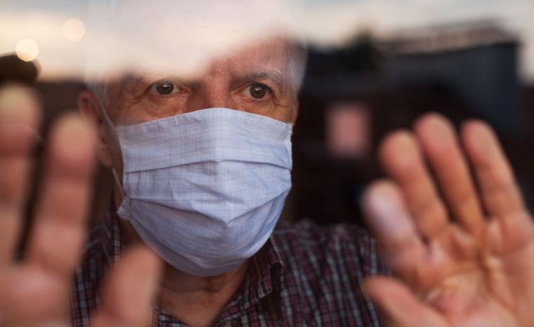 Un hombre mayor con mascarilla mira a trav&eacute;s de una ventana