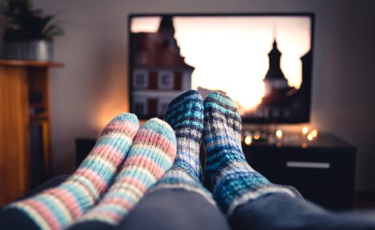 Dos personas ven la televisi&oacute;n tumbadas en un sof&aacute;