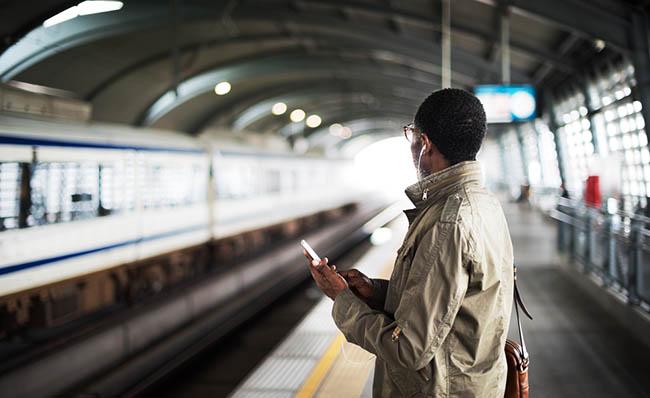 Una persona espera en un and&eacute;n la llegada de un tren mientras utiliza el m&oacute;vil