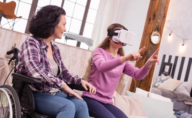 Una mujer utiliza unas gafas de realidad virtual junto a otra mujer sentada en una silla de ruedas
