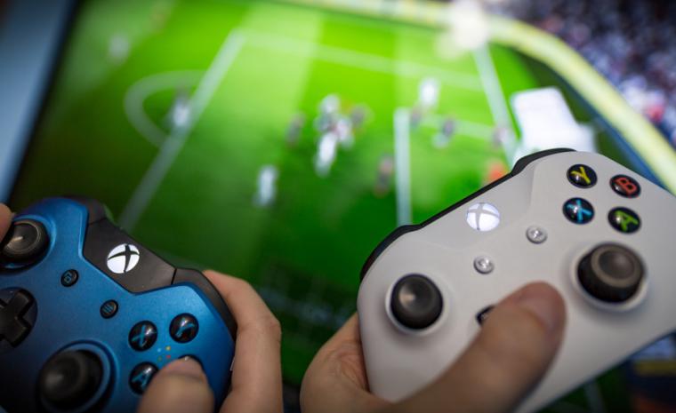 Dos j&oacute;venes sujetan sendos mandos de la Xbox One delante de un televisor