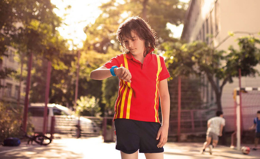 Un niño con V-Kids mira el reloj mientras juega al fútbol en la calle