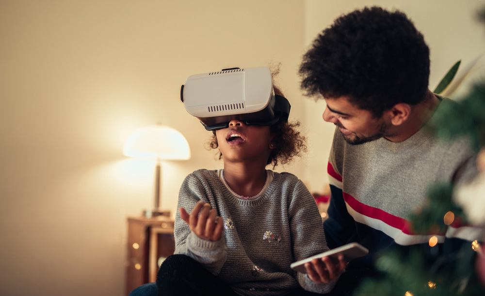 Un niño utiliza gafas de realidad virtual sentado en el regazo de su padre en una sala con adornos de Navidad